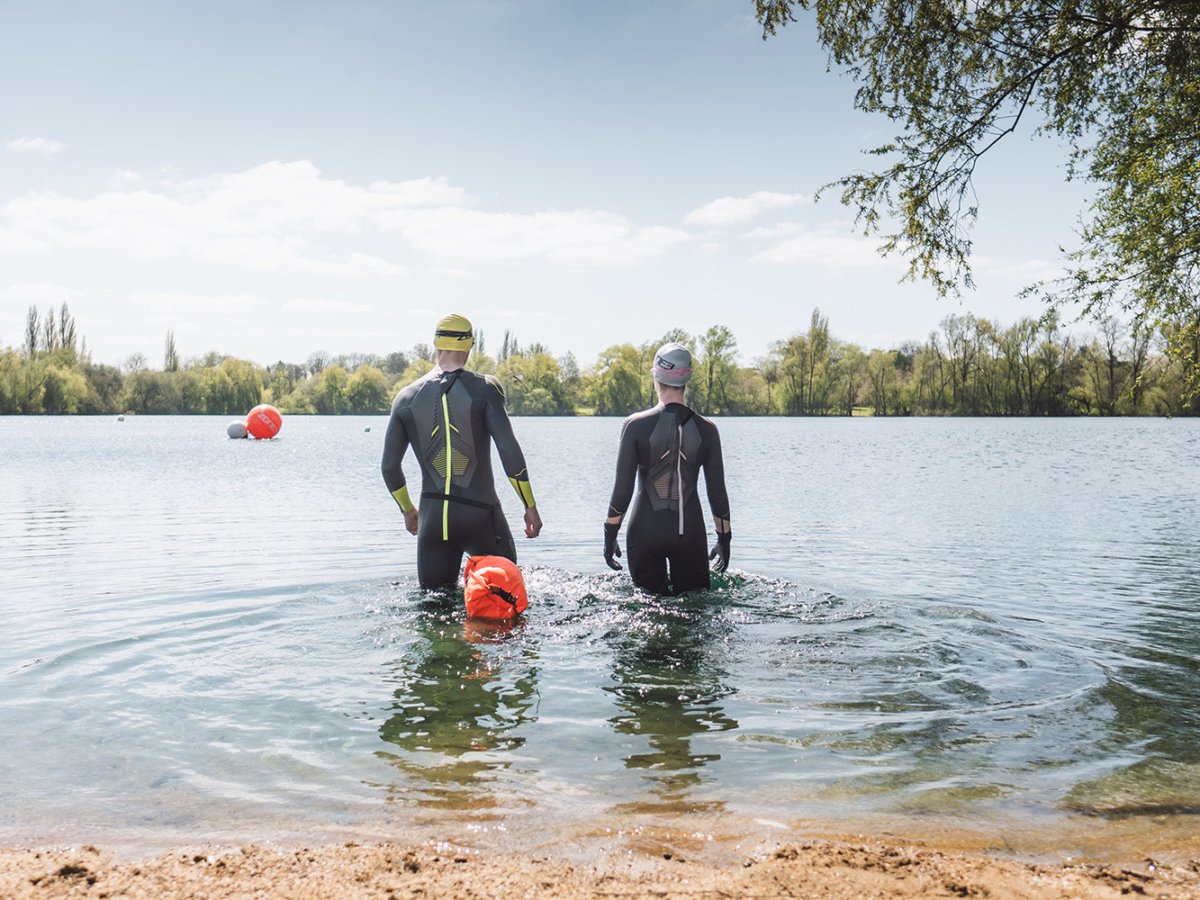 to personer går ud i en sø i våddragt med en havtaske